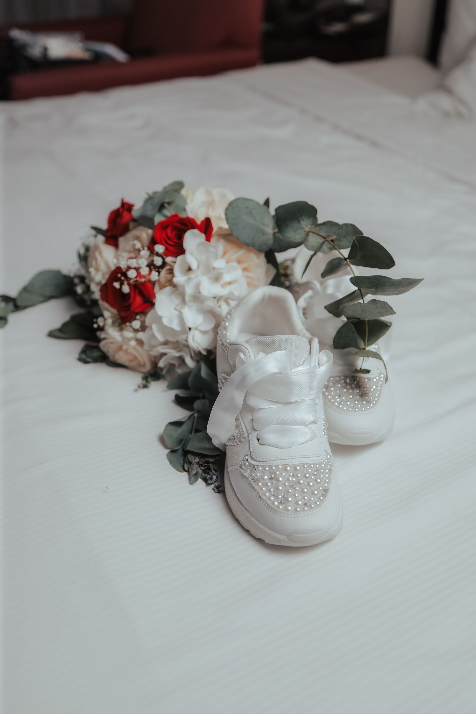 Weiße Braut-Sneaker mit Perlen und Strass neben rot-weißem Brautstrauß